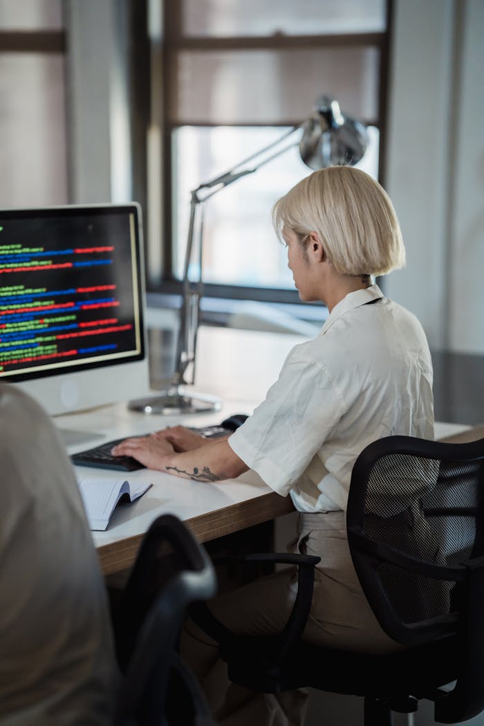 A woman working on a computer at a modern office desk, focused on her task.